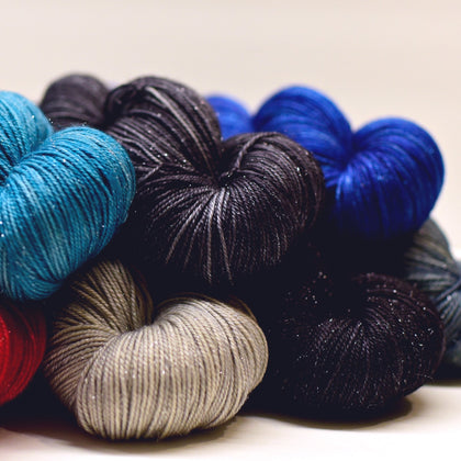 a pile of skeins of yarn in a mix of grays, blues, red, and black, all have subtle silver sparkles.